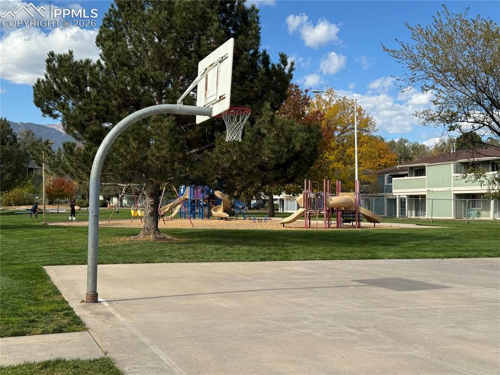 Image 26 of 27: Concrete basketball court with an adjacent playground featuring multiple sl