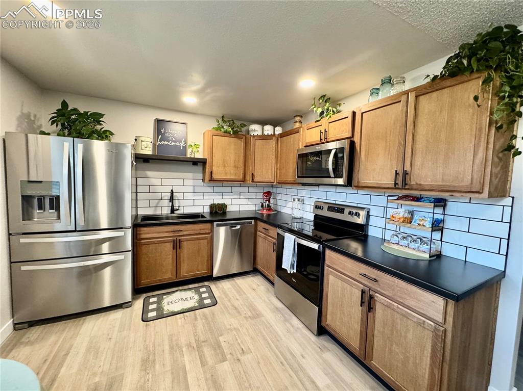Image 7 of 27: Kitchen featuring wood-finish cabinetry, black countertops, and a white sub
