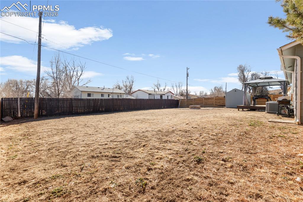 Image 32 of 32: Fenced backyard with a gazebo, a residential view, and a storage unit