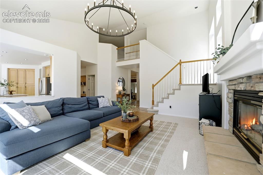 Image 13 of 50: Two-story living area with a stone-clad fireplace and white mantel, a grand