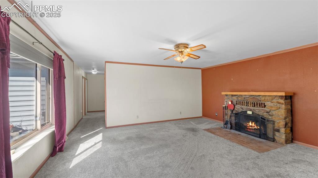 Image 14 of 33: Unfurnished living room featuring a stone fireplace, crown molding, carpet,