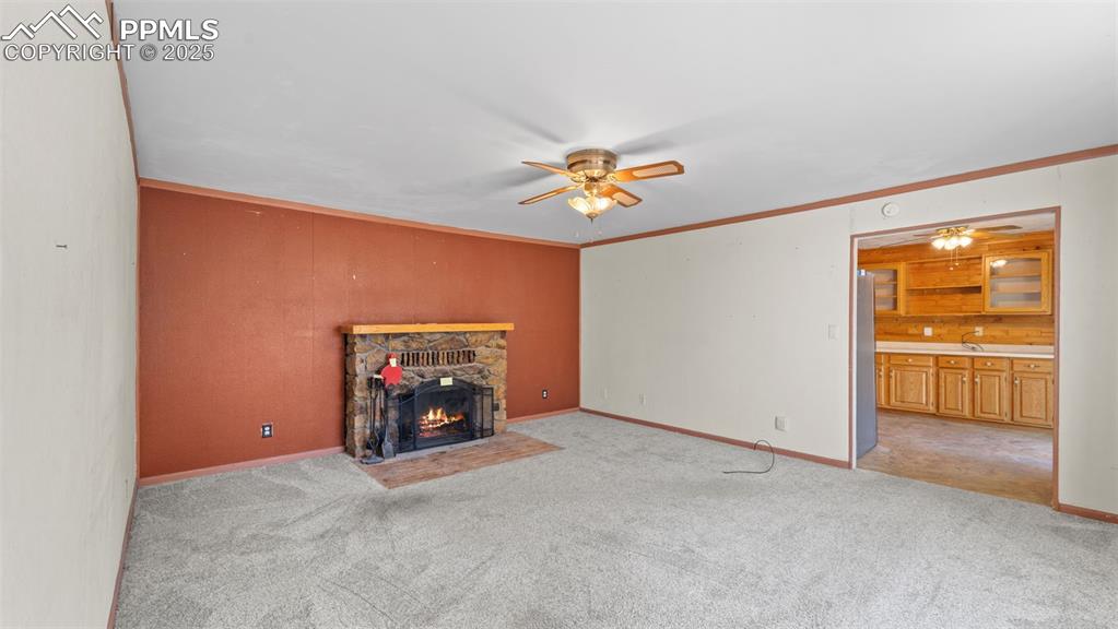 Image 23 of 33: Unfurnished living room featuring a stone fireplace, a ceiling fan, crown m