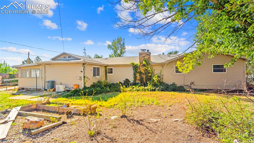 Image 25 of 33: Rear view of house featuring a vegetable garden and a chimney