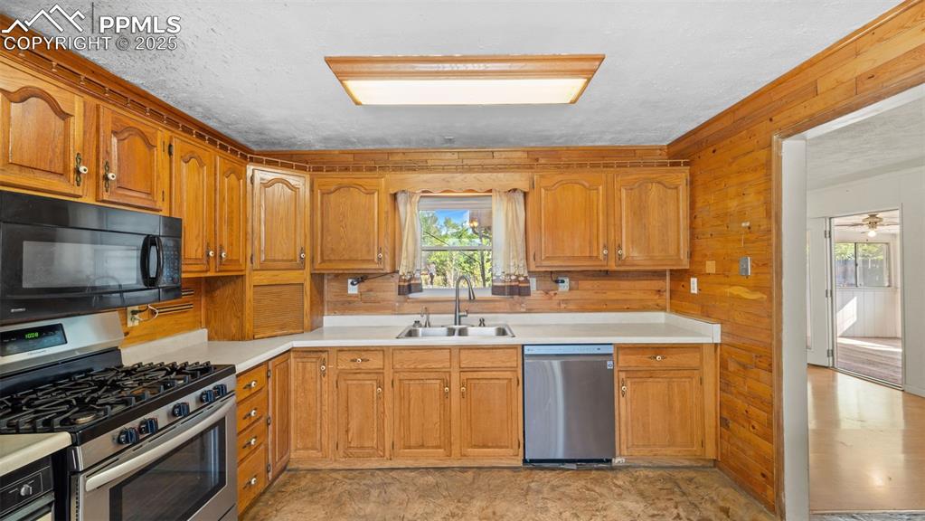 Image 6 of 33: Kitchen with appliances with stainless steel finishes, brown cabinetry, woo