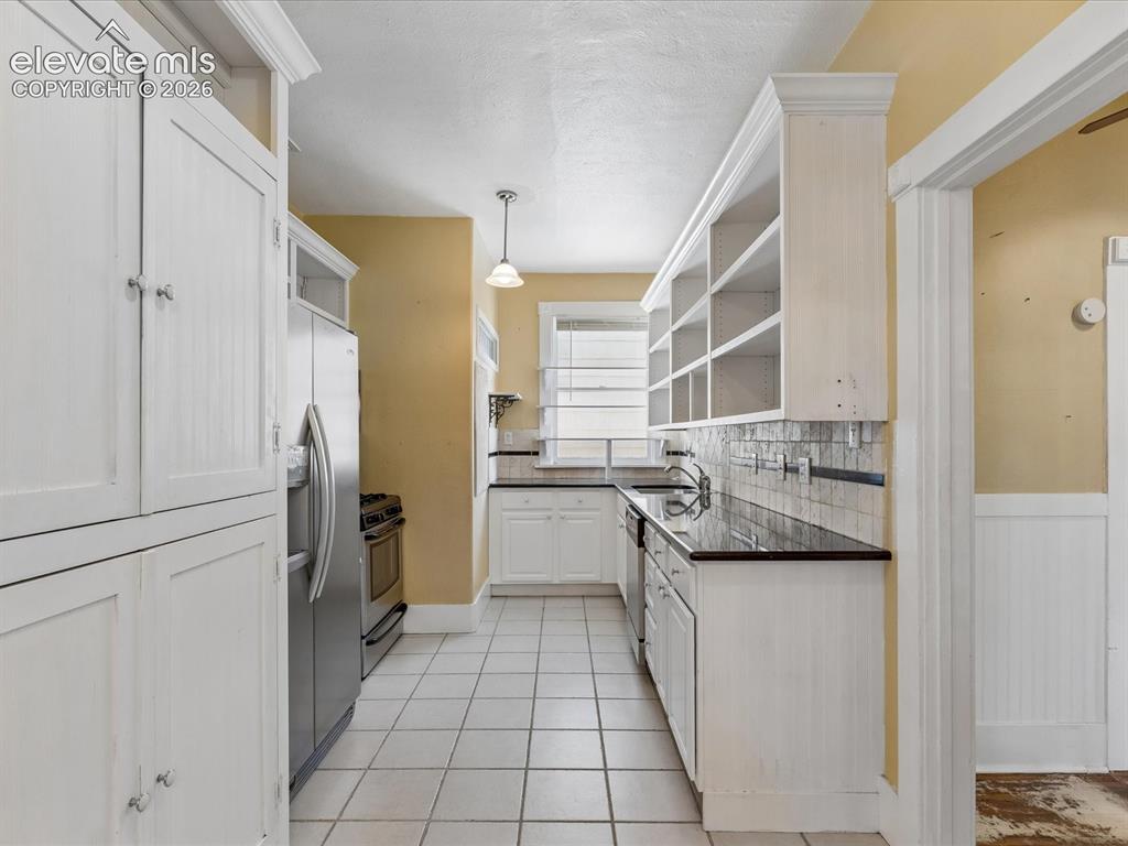 Image 11 of 35: Kitchen featuring white cabinetry, tile flooring, dark countertops, a stain