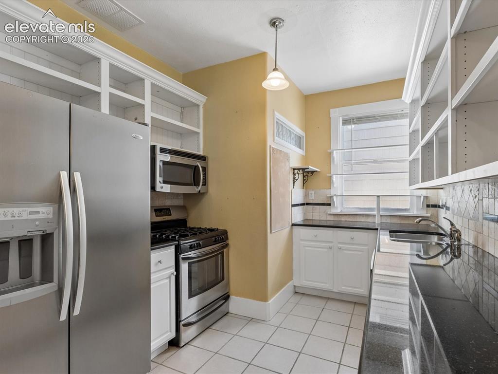 Image 12 of 35: Galley kitchen featuring white cabinetry, stainless steel appliances, black