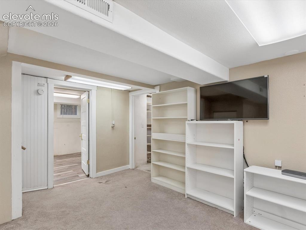 Image 19 of 35: Carpeted room featuring exposed ceiling beams, a wall-mounted television, a