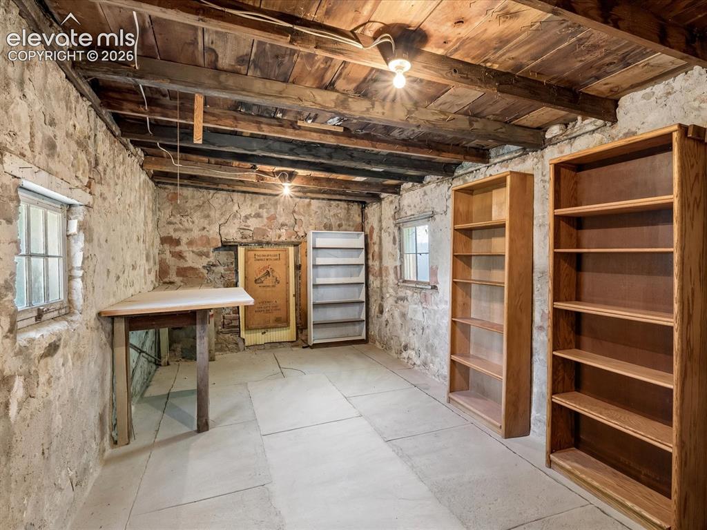 Image 24 of 35: Exposed wood-beam ceiling, stone walls, and concrete flooring define this s
