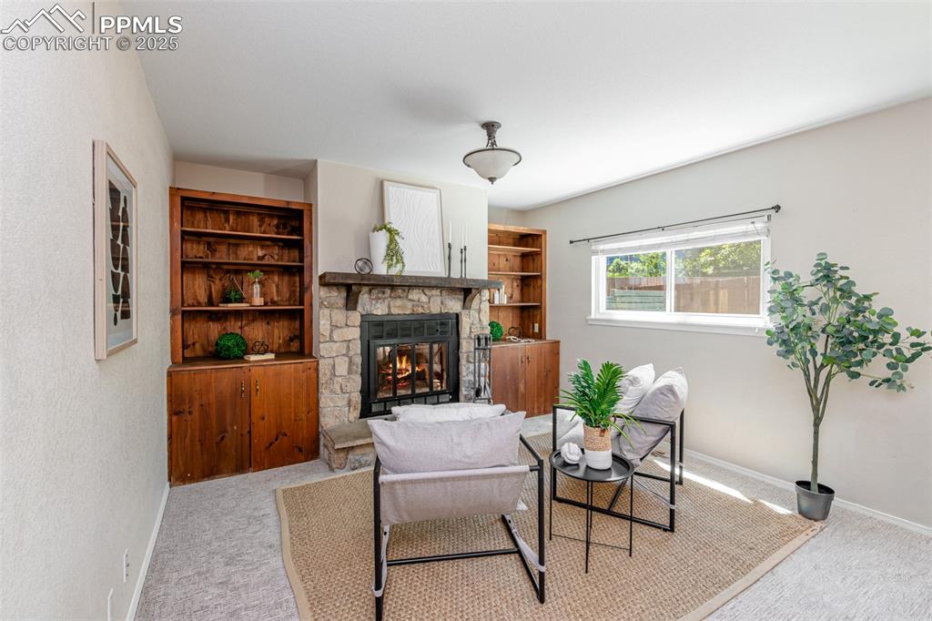 Image 14 of 38: Carpeted living area featuring a stone fireplace and baseboards