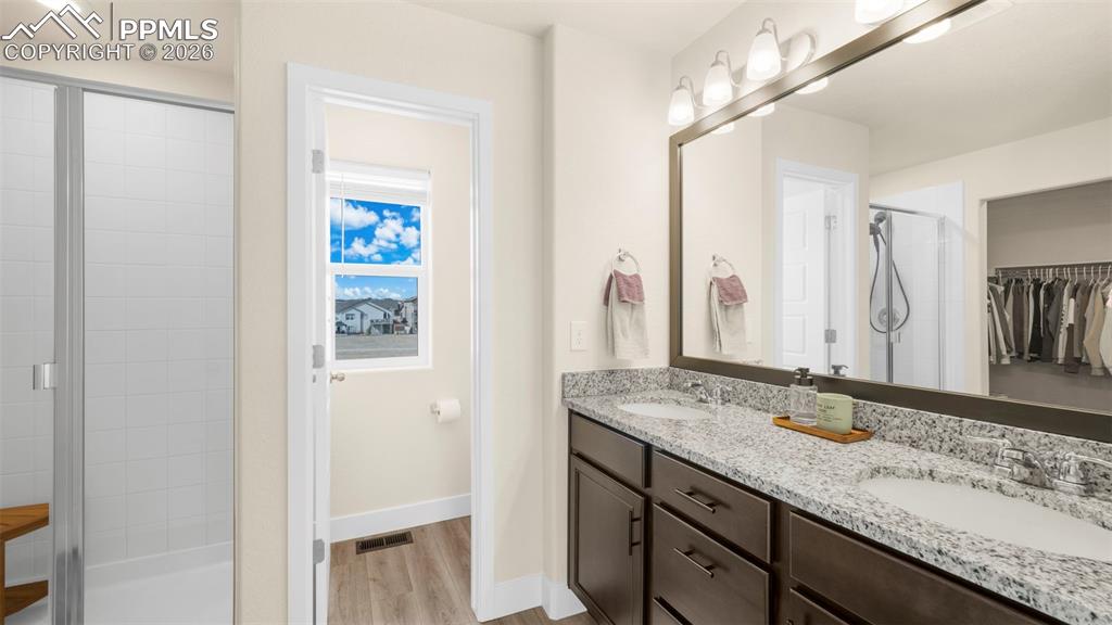 Image 25 of 43: Full bathroom featuring double vanity, a walk in closet, a stall shower, an