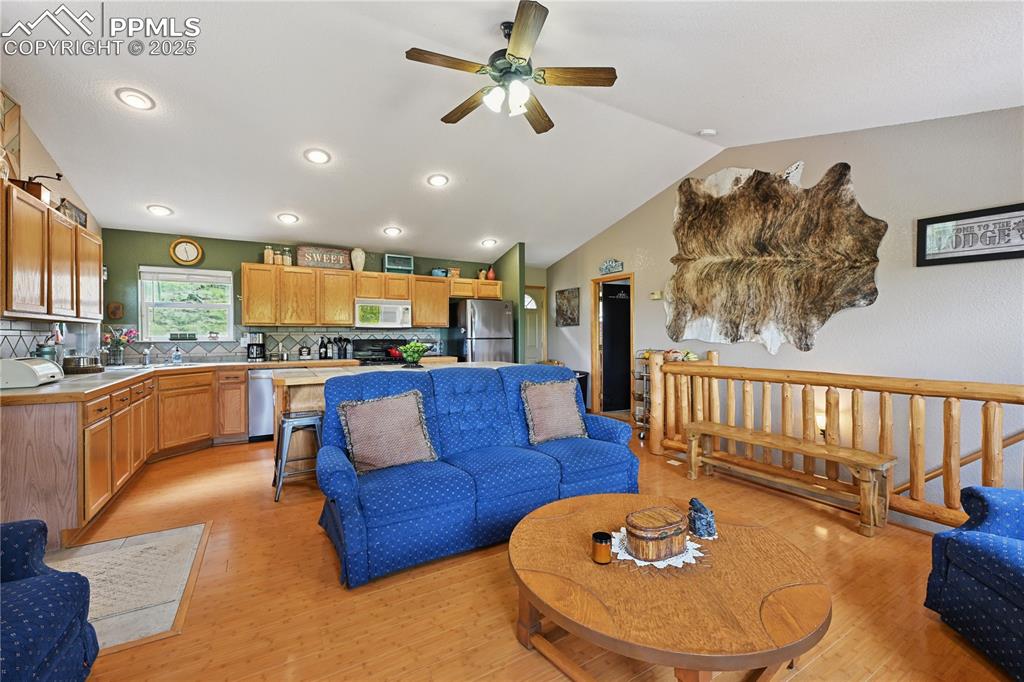 Image 23 of 34: Living area featuring light wood-type flooring, a ceiling fan, vaulted ceil