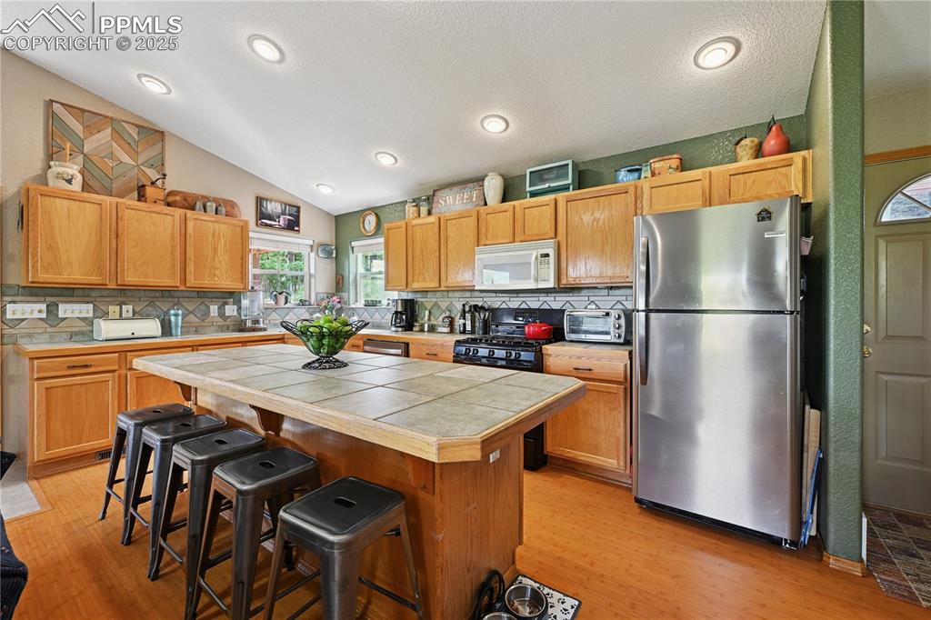 Image 26 of 34: Kitchen with lofted ceiling, decorative backsplash, freestanding refrigerat