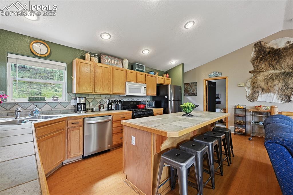 Image 28 of 34: Kitchen with vaulted ceiling, decorative backsplash, appliances with stainl