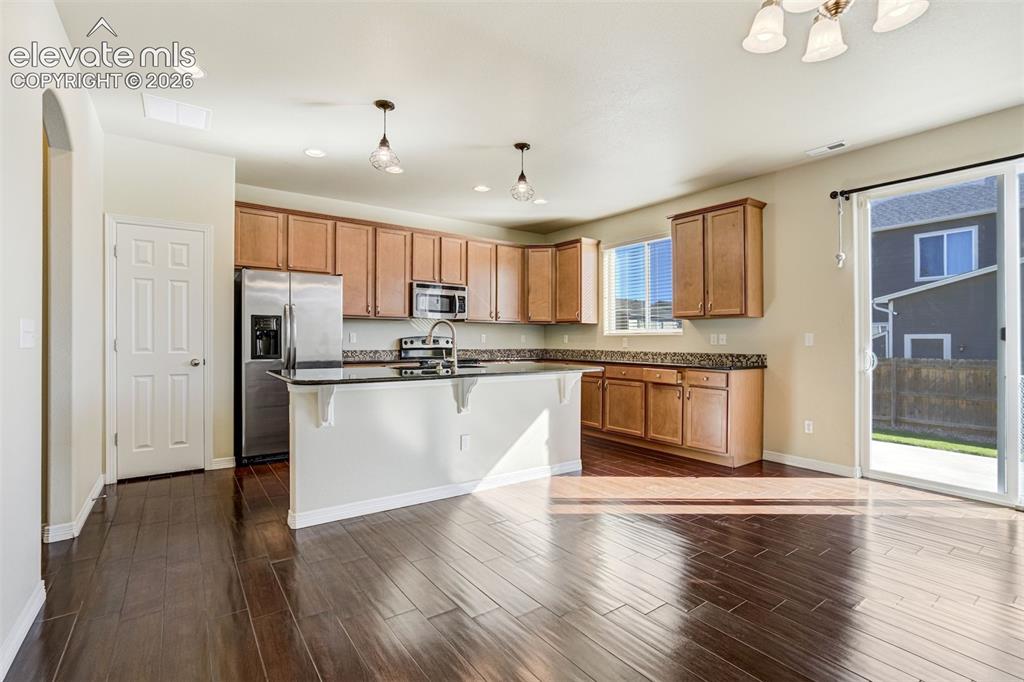 Image 16 of 49: Rich wood-finish flooring, warm wood cabinetry, dark countertops, and stain