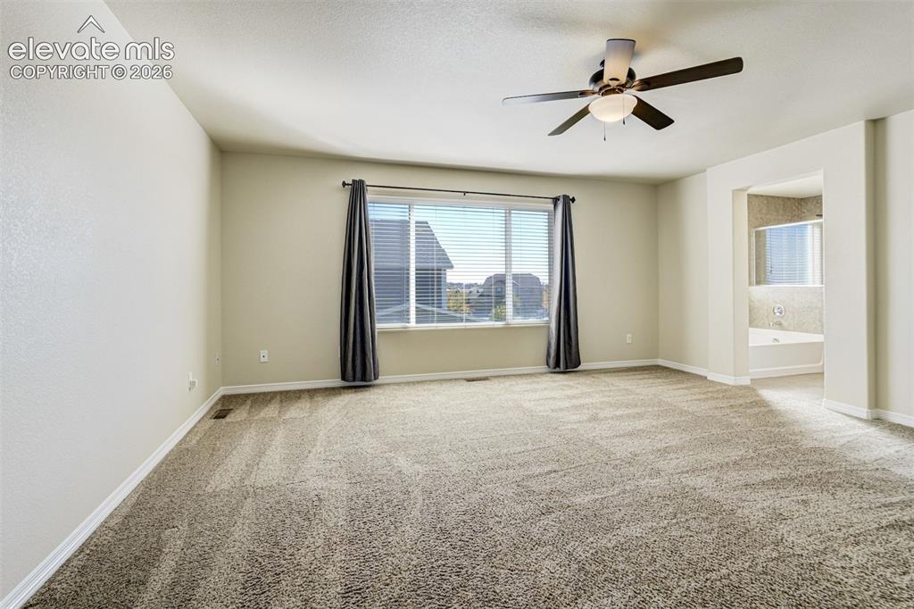 Image 25 of 49: Spacious room with plush carpeting, ceiling fan, large window, and an arche