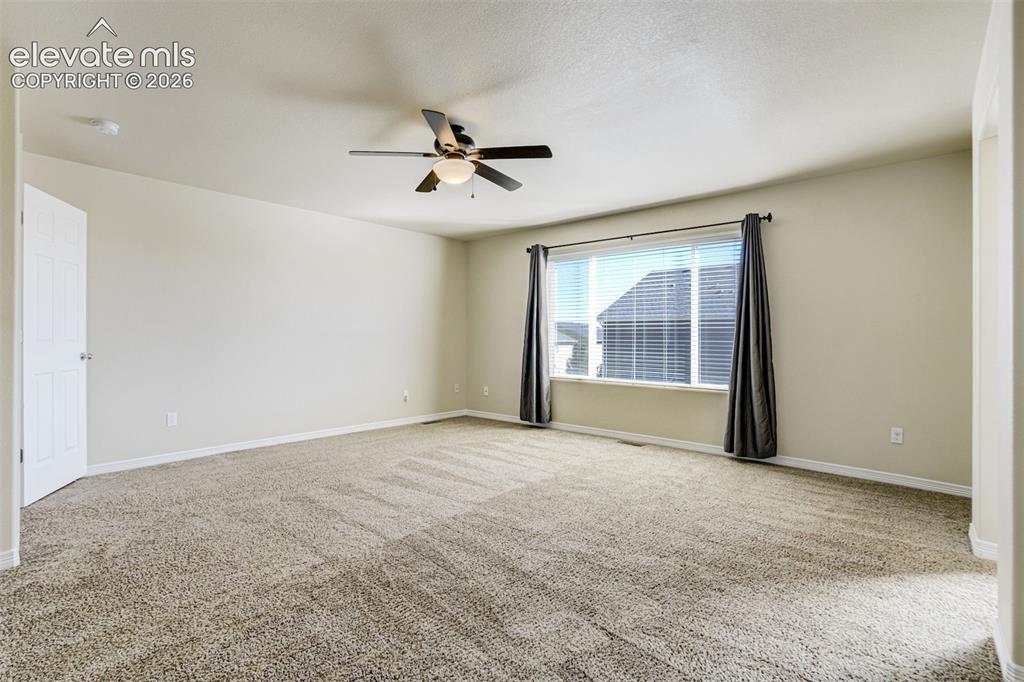 Image 26 of 49: Spacious primary living area featuring neutral carpeting, ceiling fan with