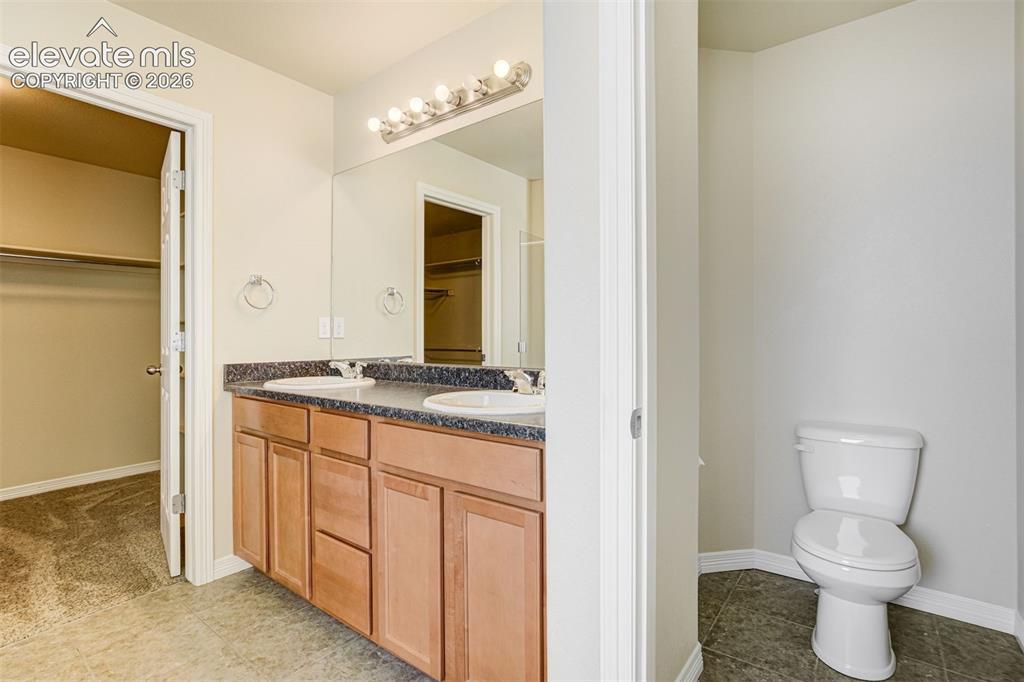 Image 28 of 49: Dual sink vanity with wood-finish cabinetry, dark speckled countertop, and