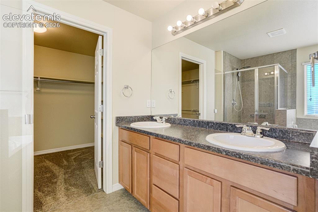 Image 29 of 49: Double vanity with two vanity sinks, wood-finish cabinetry, and dark stone-