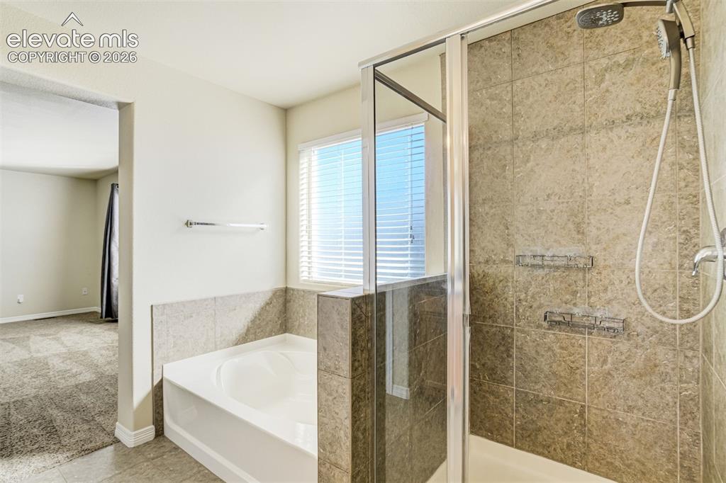 Image 31 of 49: Glass-enclosed shower with a multi-function showerhead, tiled walls, and bu