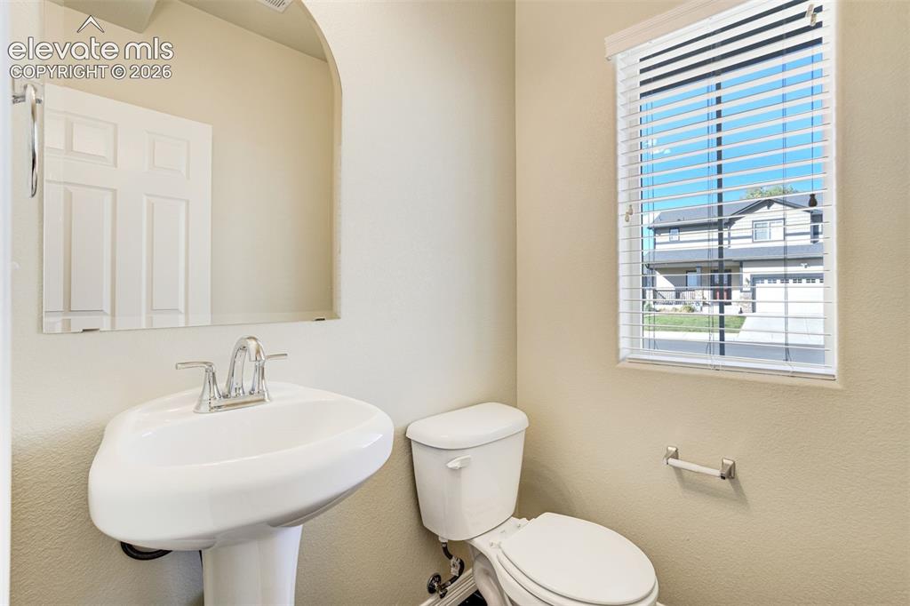Image 38 of 49: Pedestal sink with chrome faucet, wall-mounted mirror, white window blinds,