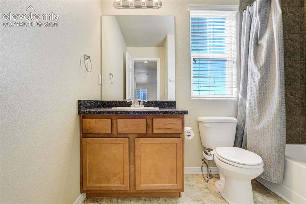 Image 39 of 49: Vanity with a dark countertop and a white basin sink, wood-finish cabinetry