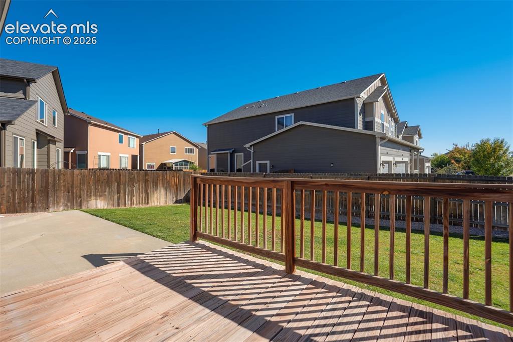 Image 42 of 49: Wood-finish deck with a matching wood railing, concrete patio, and a grass