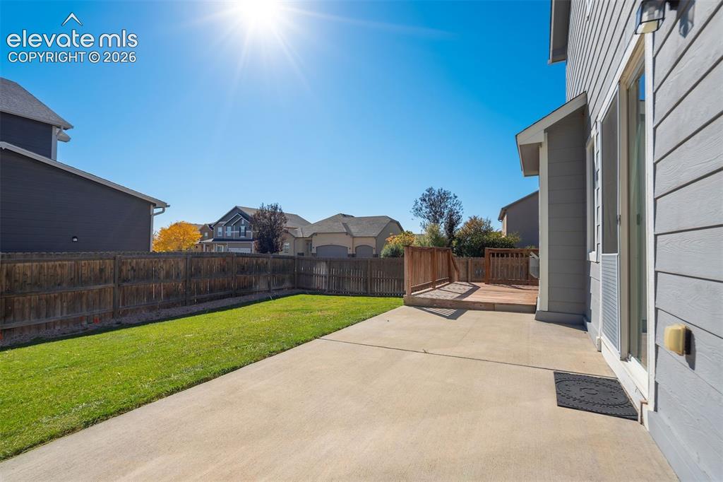 Image 46 of 49: Private backyard with a wooden fence, concrete patio, and an elevated woode