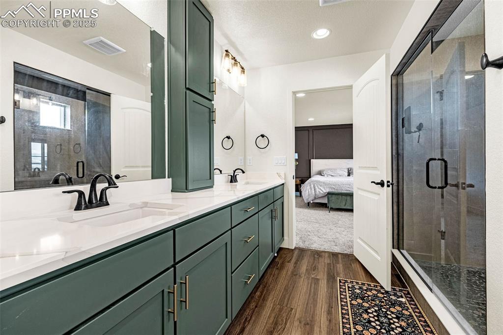 Image 17 of 32: Ensuite bathroom with double vanity, a stall shower, dark wood-type floorin