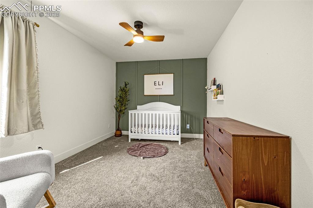 Image 18 of 32: Bedroom with a crib, carpet flooring, and a ceiling fan