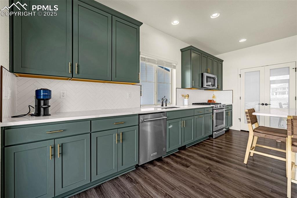 Image 4 of 32: Kitchen with green cabinetry, decorative backsplash, dark wood-style floors