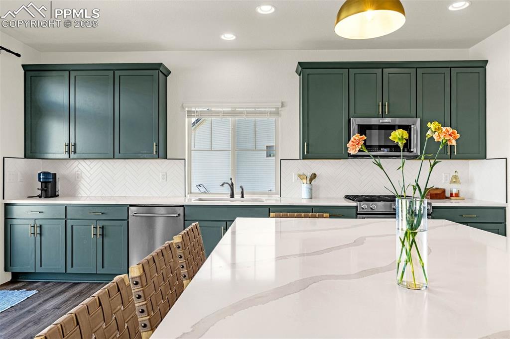 Image 5 of 32: Kitchen with green cabinets, recessed lighting, tasteful backsplash, light