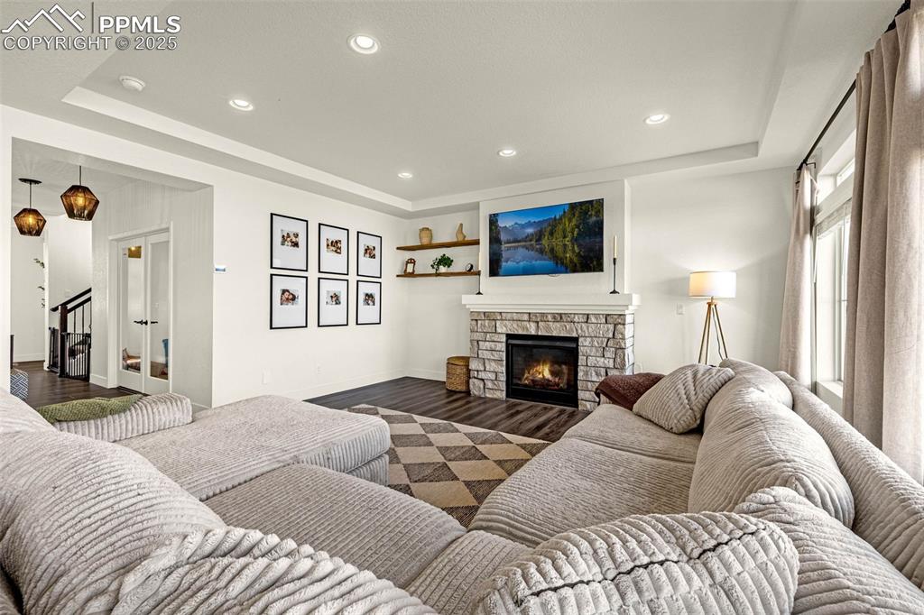 Image 8 of 32: Living area with a tray ceiling, recessed lighting, a stone fireplace, and