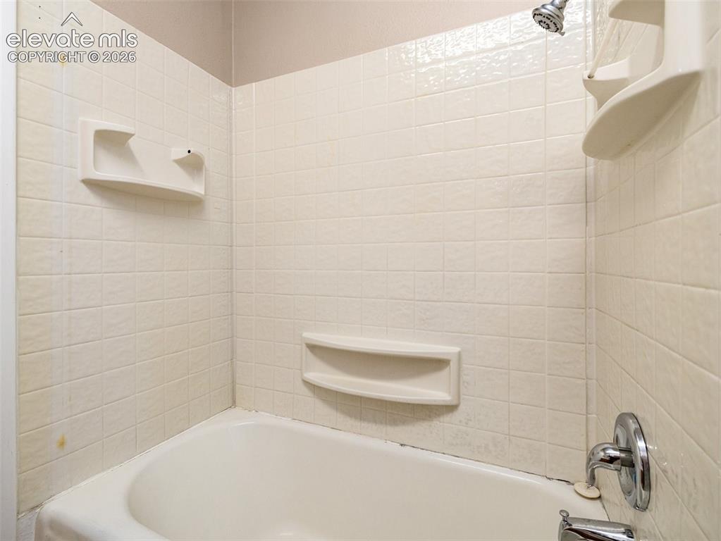 Image 12 of 22: Tub and shower combination with tiled surround, chrome showerhead, and buil