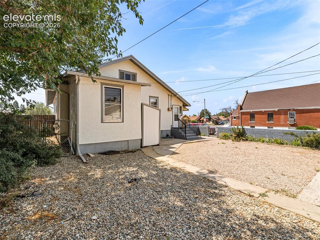 Image 22 of 22: Stucco exterior with a pitched roofline, bordered by a gravel yard and a co