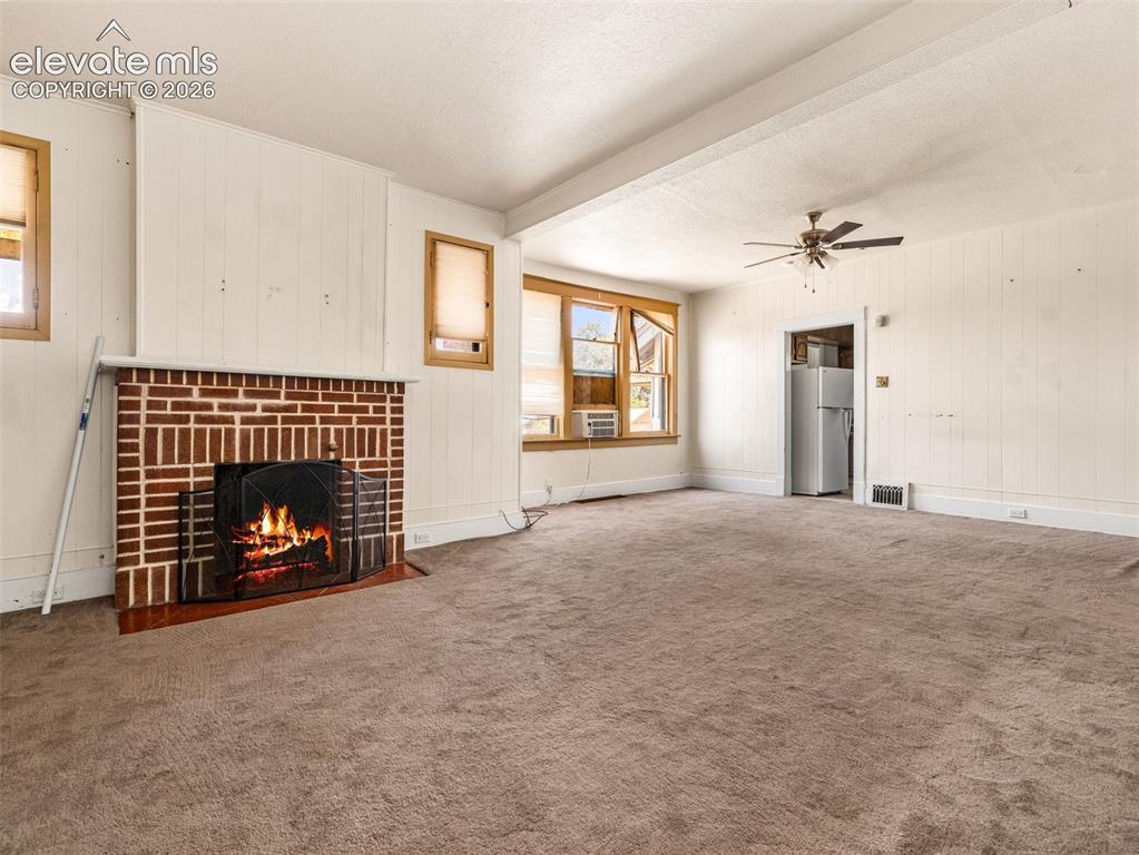 Image 3 of 22: Brick fireplace with hearth, ceiling fan, and carpeted flooring