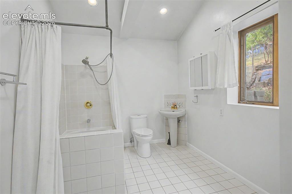 Image 16 of 27: Bathroom featuring white ceramic tile flooring, pedestal sink with tiled ba