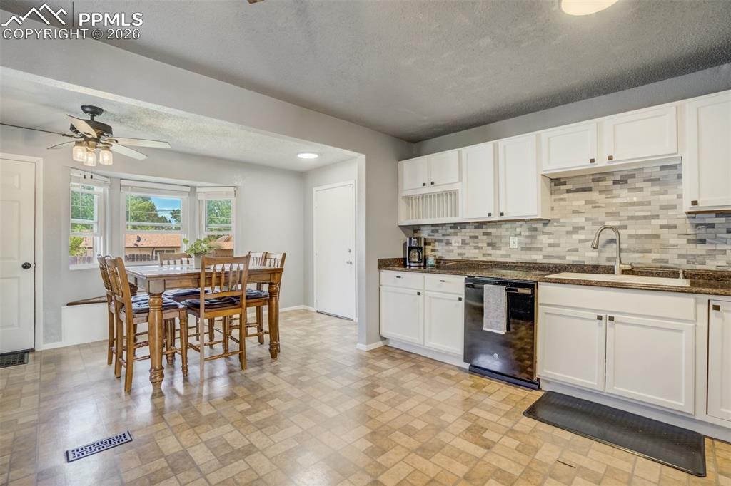 Image 9 of 44: Kitchen with white cabinetry, dishwasher, a ceiling fan, dark stone counter