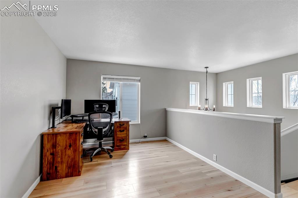 Image 21 of 46: Office space with light wood-style flooring, a chandelier, and a textured c