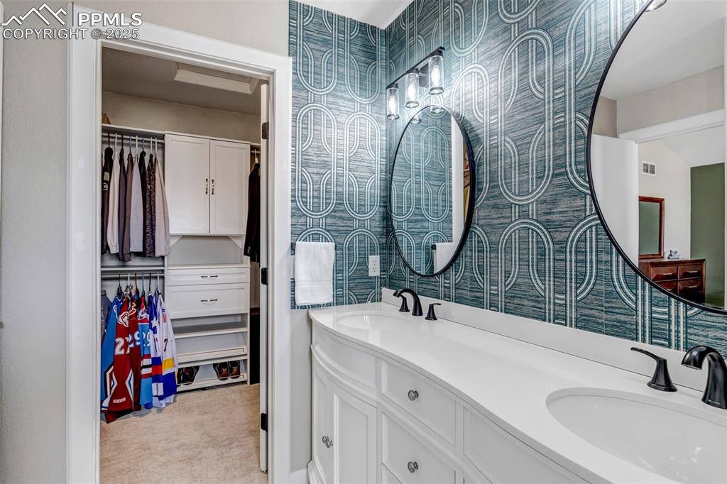 Image 27 of 46: Bathroom with wallpapered walls, double vanity, and a walk in closet
