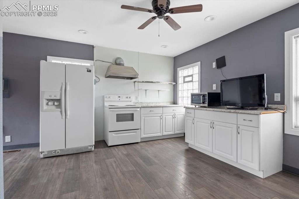 Image 8 of 14: Kitchen with white appliances, white cabinetry, ceiling fan, wall chimney e