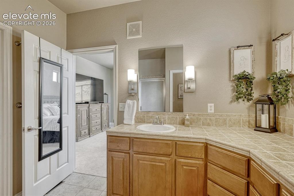 Image 24 of 41: Bathroom vanity with a double basin sink, tile countertop, and wood-finish
