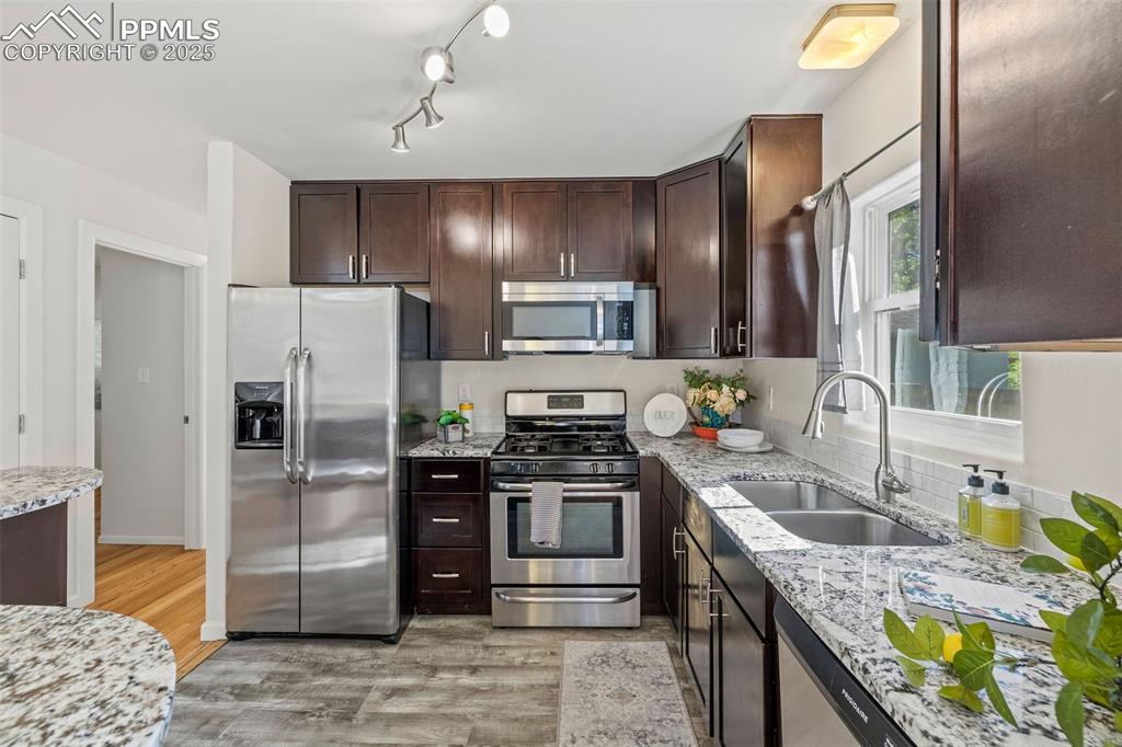 Image 12 of 39: Kitchen with stainless steel appliances, light wood-style floors, dark brow