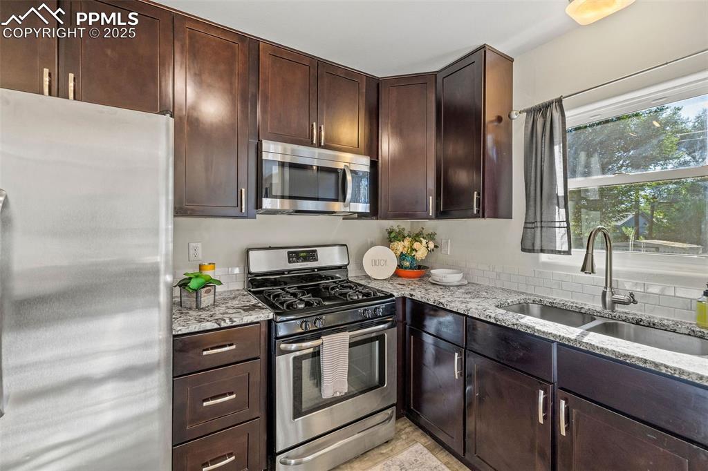Image 14 of 39: Kitchen featuring stainless steel appliances, light stone counters, and dar