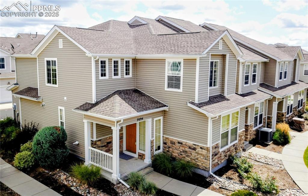 Caption: View of front of house with roof with shingles, stone siding, and covered porch