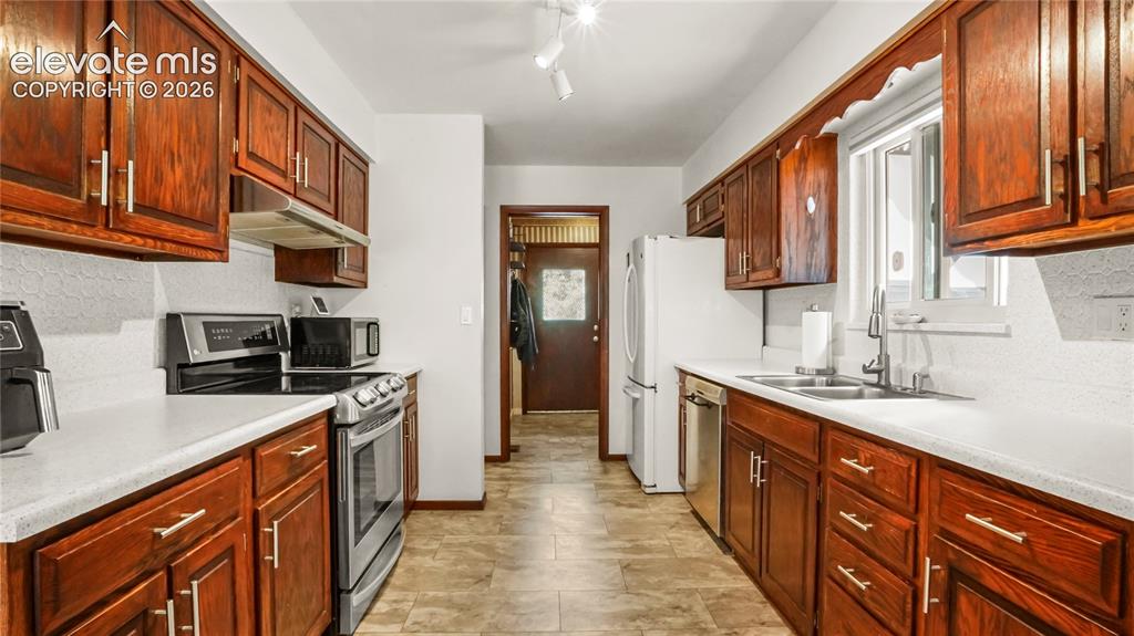 Image 19 of 40: Galley kitchen featuring wood cabinetry, white countertops, and appliances