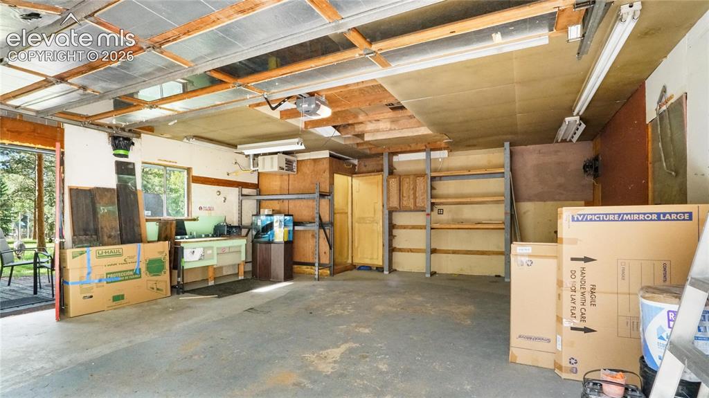 Image 34 of 43: Garage featuring a built-in workbench, exposed beam ceiling, fluorescent li