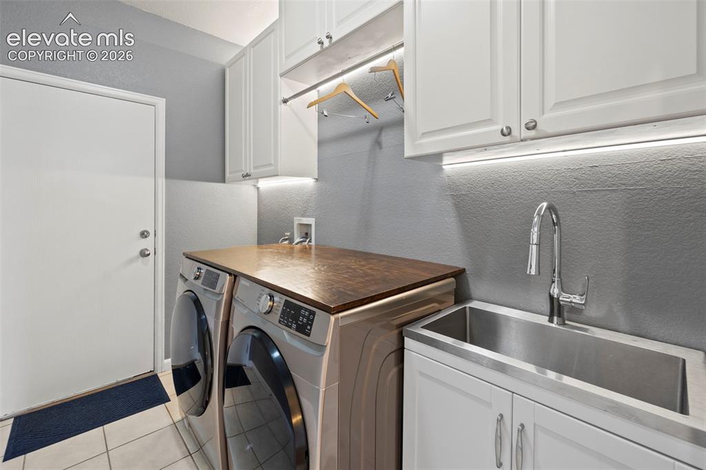 Image 16 of 50: Convenient main floor laundry room with utility sink, tile flooring, cabine