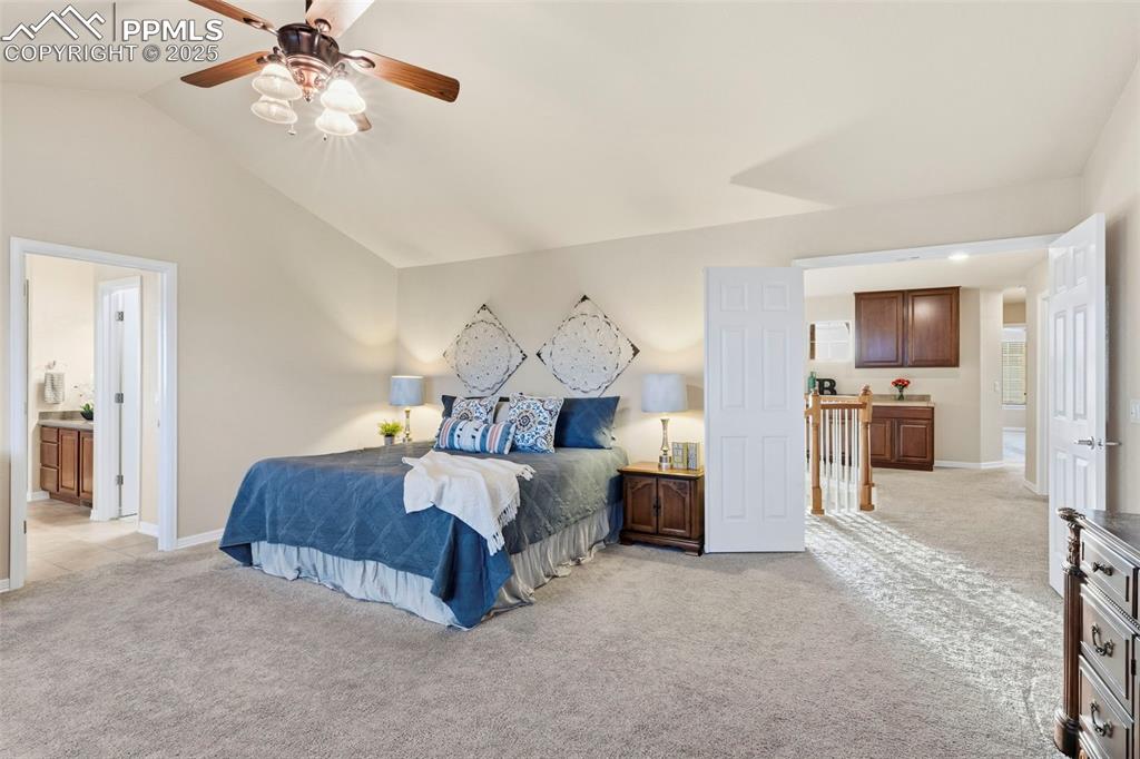 Image 22 of 46: Bedroom with light carpet, lofted ceiling, ceiling fan, and ensuite bathroo