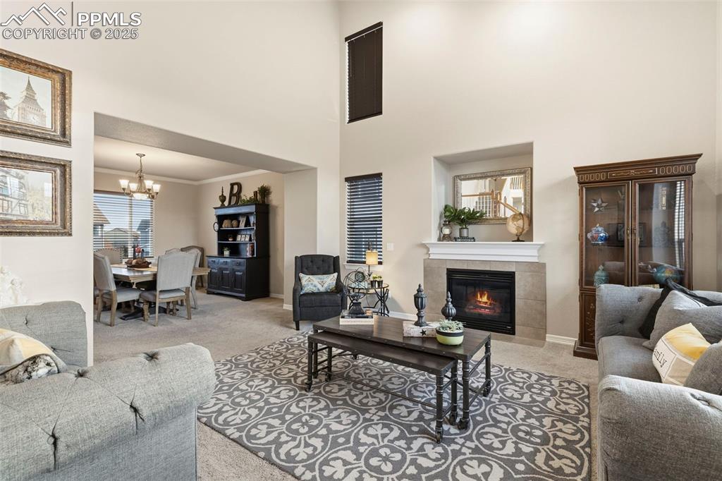 Image 8 of 46: Carpeted living room featuring a fireplace, a high ceiling, and a display n