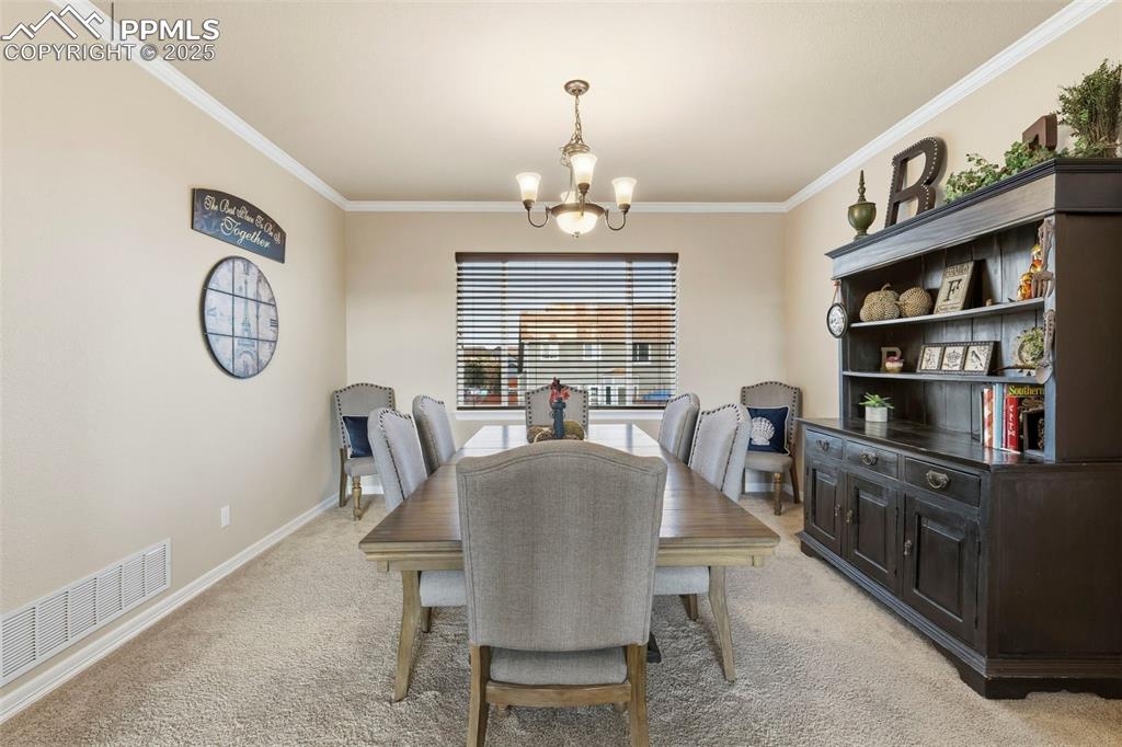 Image 9 of 46: Dining space featuring light colored carpet, ornamental molding, and a chan